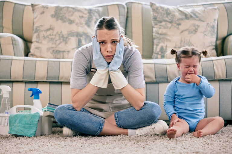 Shot of a woman looking stressed while busy with chores and sitting with a crying baby at home
