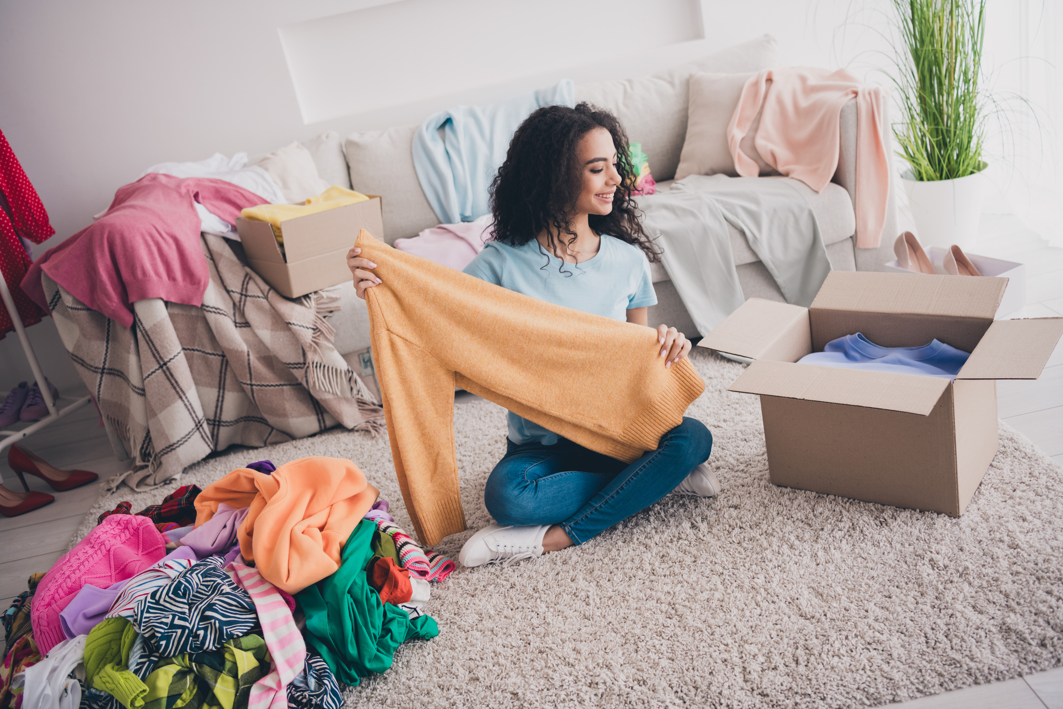 woman sitting on the living room floor decluttering her clothes and putting the donate in boxes